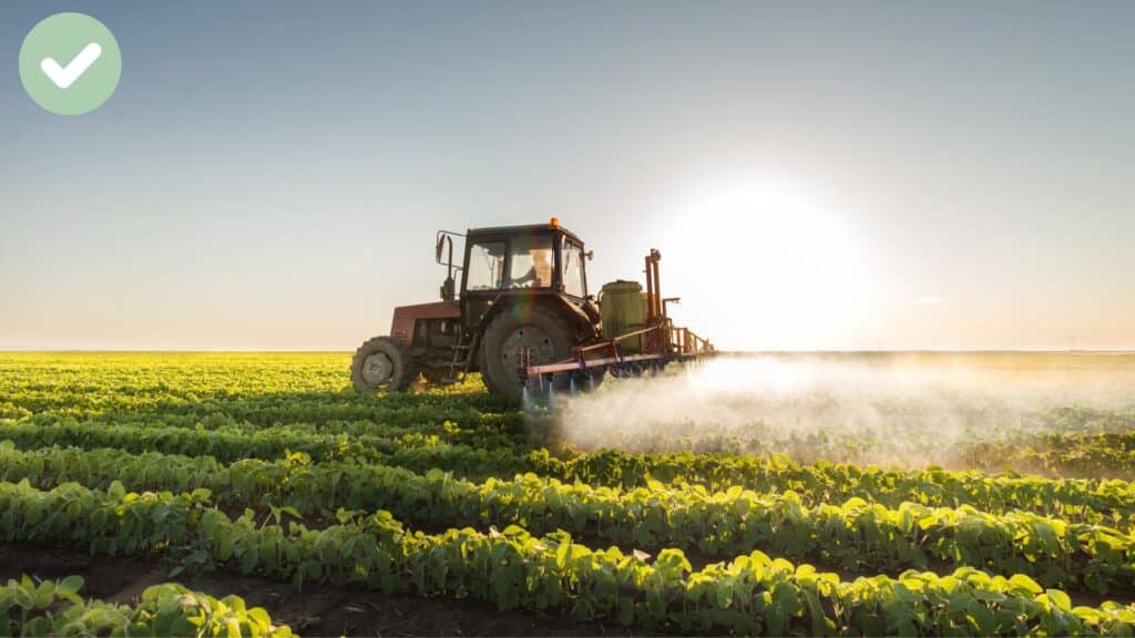 Tractor spraying crops in a field at sunset.